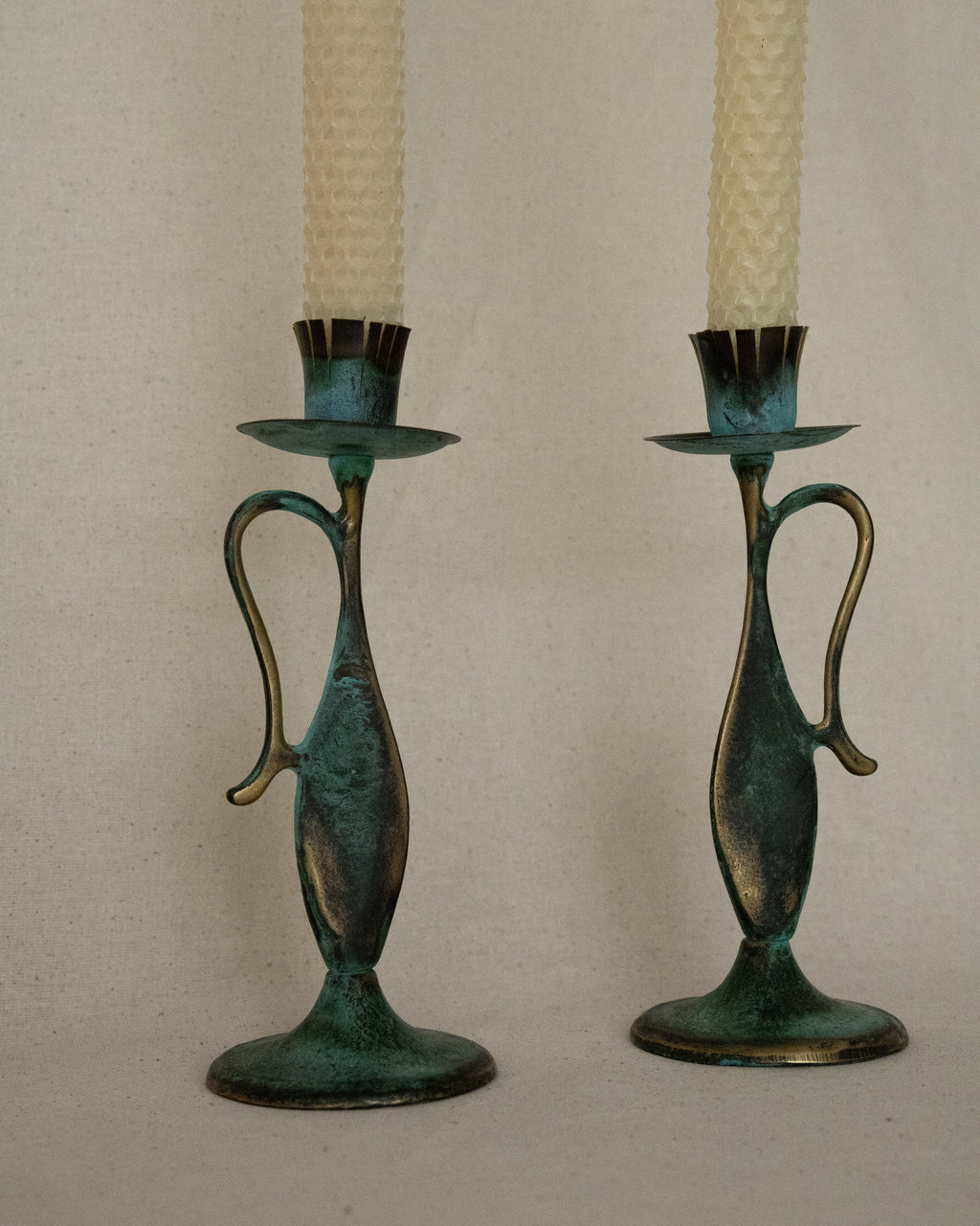 Pair of brass intentional verdigris single candle holders in the shape of vessels with handles